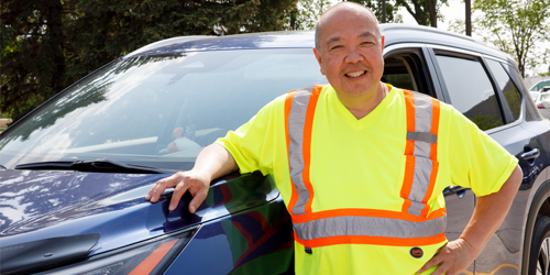 A man leaning on a vehicle with one hand and has the other hand on his hip.